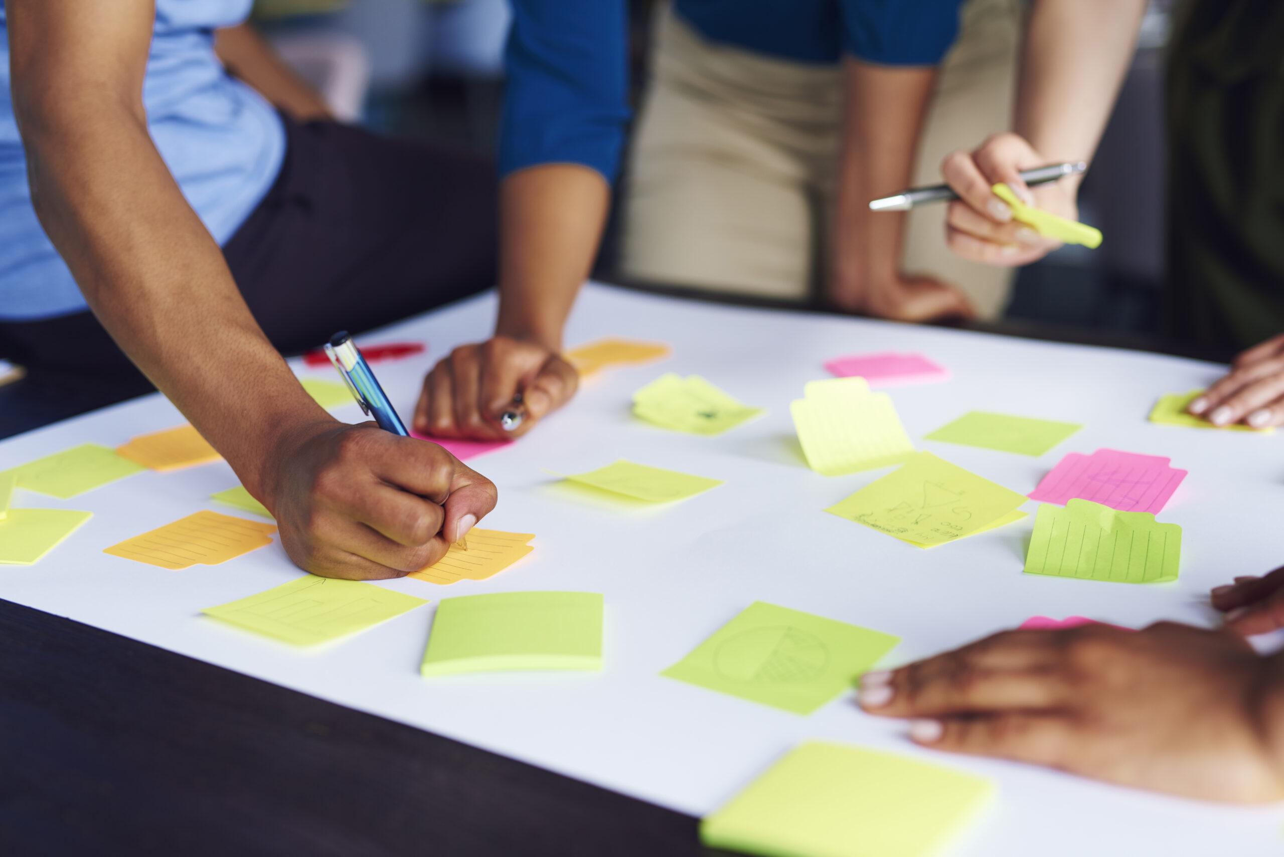 Group of people writing on bright sticky notes spread across a white table during a brainstorming session.