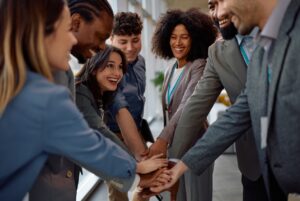 Trust and Flexibility build better teams Diverse team of six adults in business attire stacking hands in the center to show teamwork and celebration in an office setting.