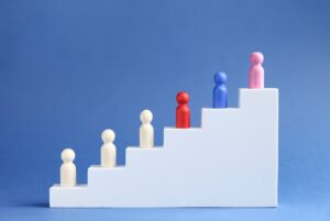 High_performing_sales_teams_flipped_1264x848 Six colorful peg figures ascending a white staircase against a blue background, symbolizing growth and progression.