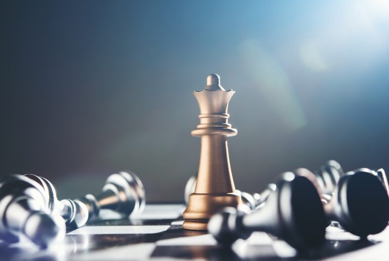Gold king chess piece stands upright on a chessboard, surrounded by fallen pieces, symbolizing leadership and strategic dominance in a game.